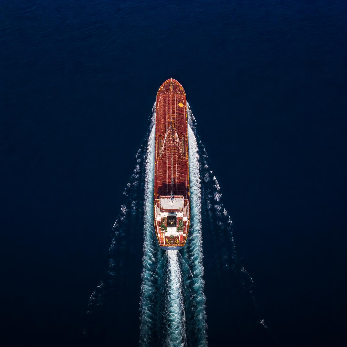 Large commercial vessel leaving a clean white wake through deep blue open water